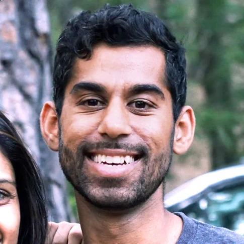 Headshot of Arun. A man with black hair and beard wearing a blue t-shirt 