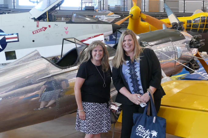 Two women pose in front of a plane