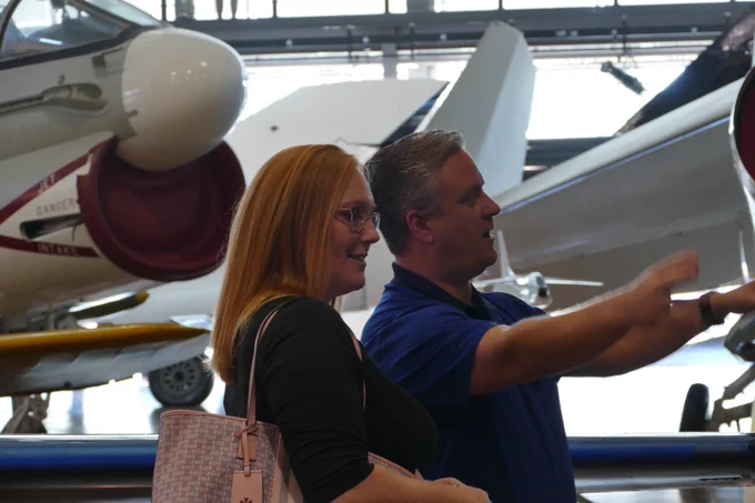 A man and a woman smile and conversate, there are planes behind them