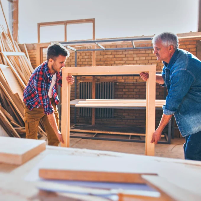 Two men holding wooden frame.