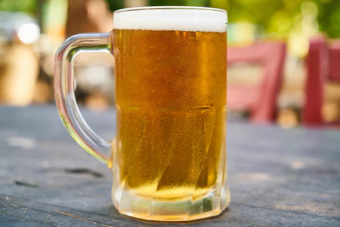A mug of cold beer sitting on an outside restaurant table.