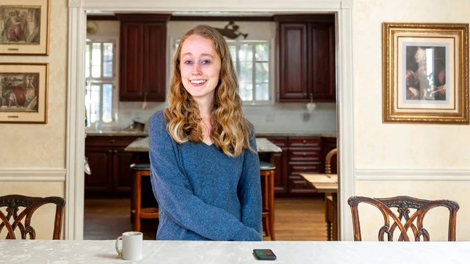 Erin Smith sitting in her family home, smiling for the camera, with her cell phone opened to the FacePrint app in front of her