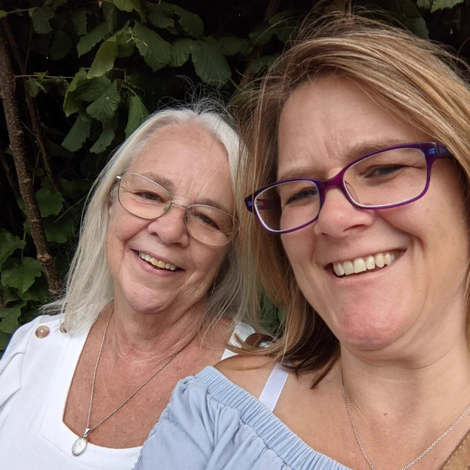 Benita (left) wearing a white top and glasses, with Marie (right) wearing blue top and glasses) both smiling to the camera.