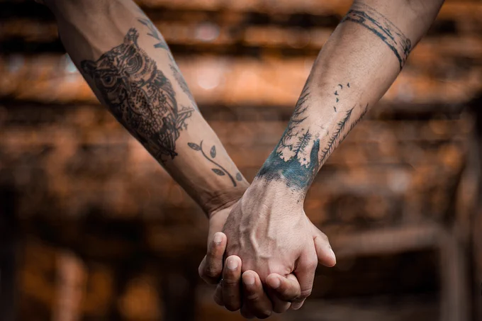Two people with tattoos on their forearms holding hands.