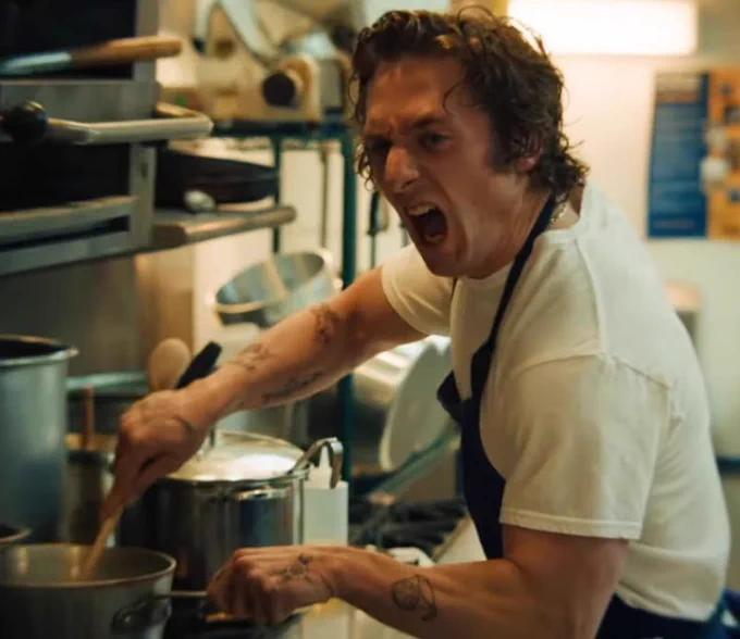 A still shot from the Hulu original show, The Bear. The actor, Jeremy Allen White, is cooking in a dirty and rundown kitchen. He’s stirring something in a pot and screaming at his coworkers. It’s very intense looking.