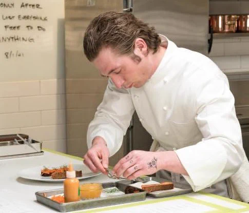 A second still shot from the Hulu original show, The Bear, and a completely opposite moment from the first photo. The actor, Jeremy Allen White, is cooking in an immaculate kitchen belonging to one of the top fine dining restaurants in the world. He looks calm, but his movements are precise and he’s totally focused on plating a stunning plate of food.