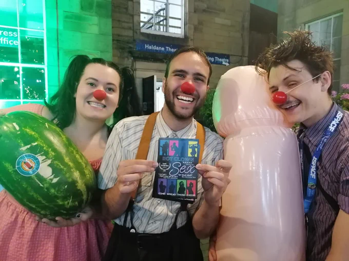 Three clowns, holding a watermelon, a flyer for the show hot clown sex and a large inflatable penis