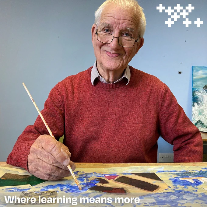 Photo of John Gray in the art studio at Orkney College UHI. John is holding a paintbrush and appears to be working on a piece of art. 