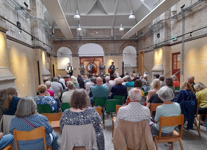 Photograph showing the Jake Leg Jug Band performing in the Old Parcels Office at Scarborough Station to a room packed full of people.