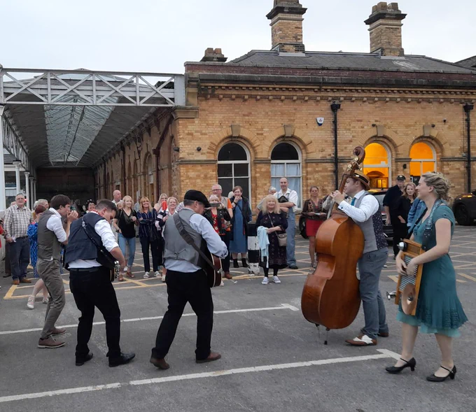 Photograph showing the Jake Leg Jug Band performing in the car park at Scarborough Station for the audience.