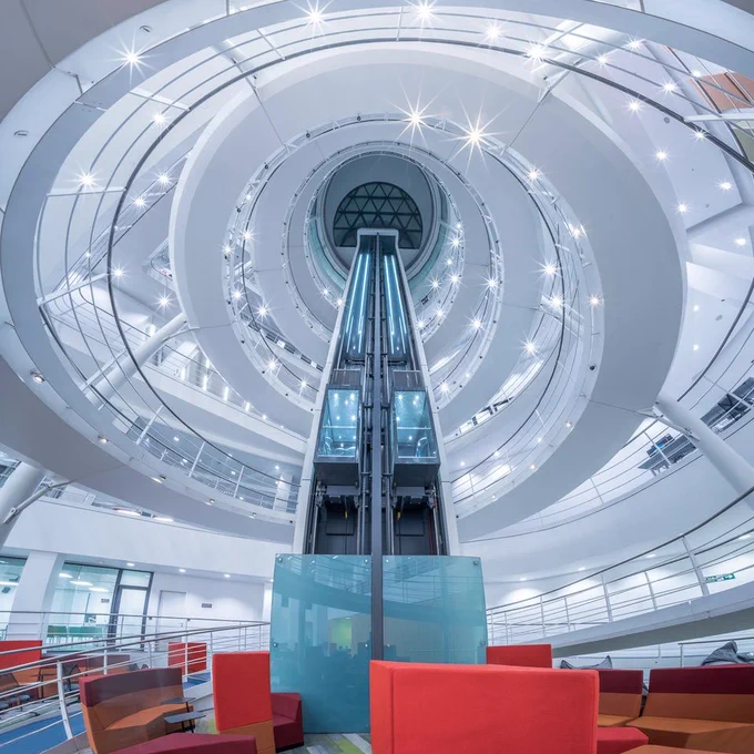 A photograph taken from the lower ground floor of LSE Library with a view up towards the dome. It includes the lift shaft and spiral staircase. The lights have been enhanced to appear as if they are shining like a star.