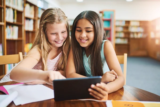 Two girls aged about 12, reading on a tablet together in a library