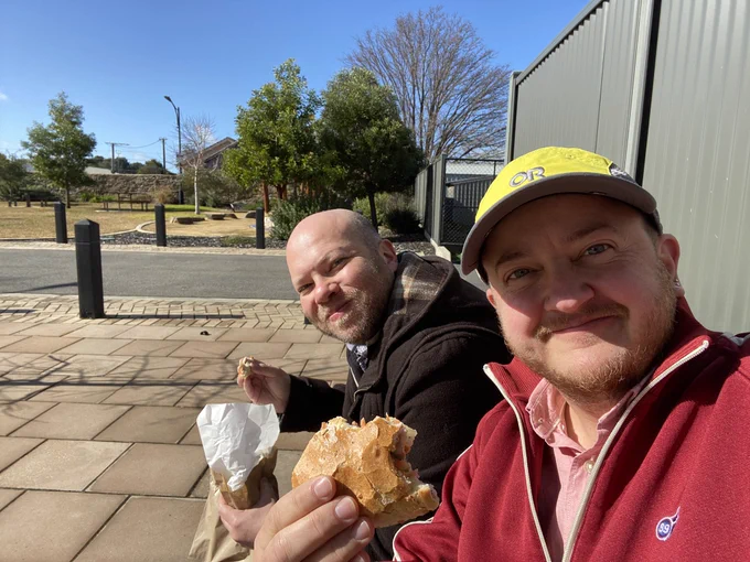 Selfie POV of two smiling people eating salad rolls in the sun