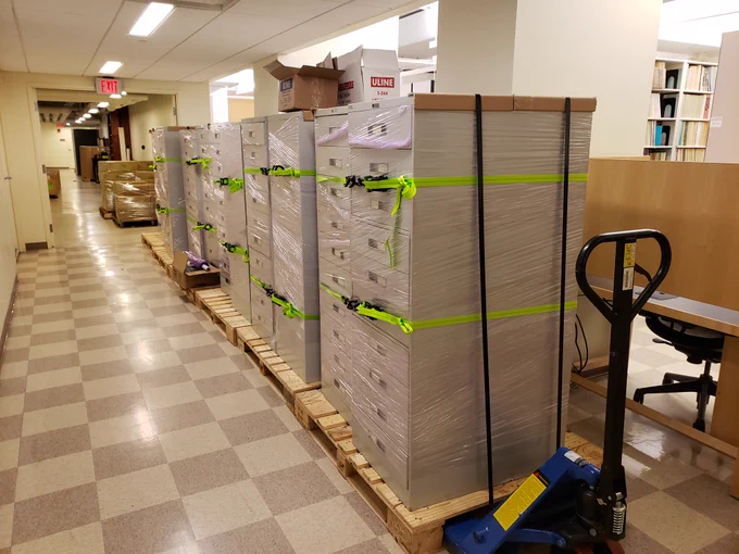 Metal filing cabinets containing microfiche documents are strapped on pallets in a library hallway at Colgate University.