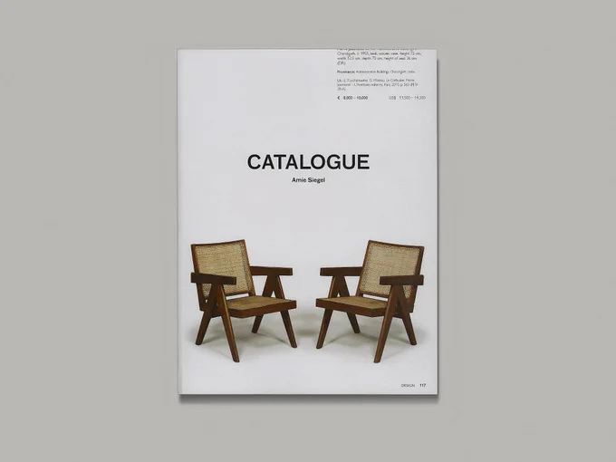 A catalogue lies on a blank grey background. The cover says ‘Catalogue’ in large capital letters and ‘Amie Siegel’ in smaller letters underneath. Below the title are two wooden armchairs with woven seats and backs, against a blank white background.