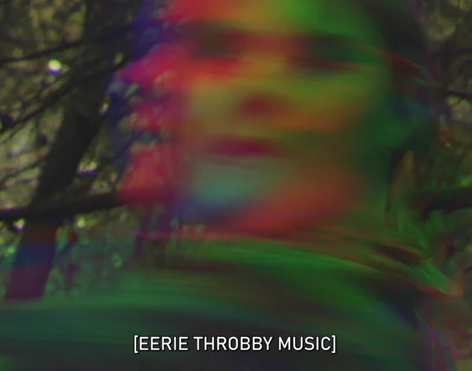 A still from The Commons showing a head shot Chloe Richardson dervish-dancing in the forest, a psychedelic image, faced blurred, colours red and green, with the caption: "EERIE THROBBY MUSIC"