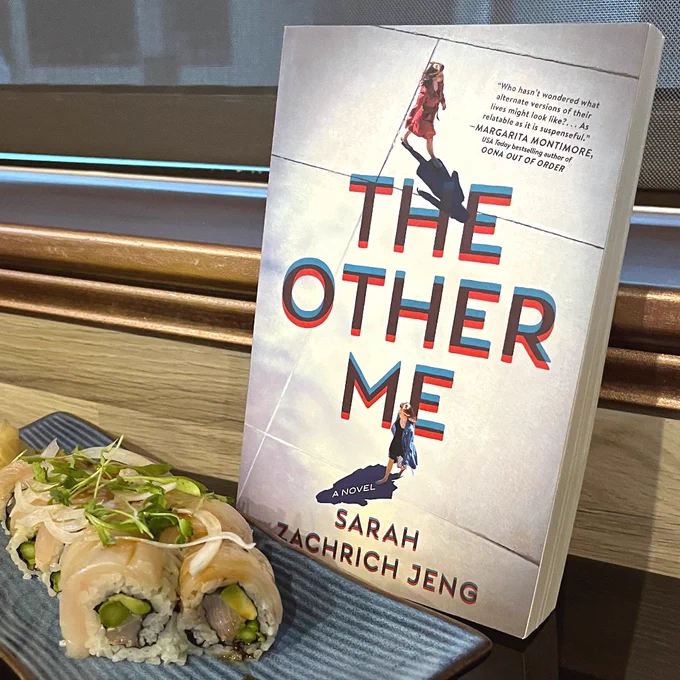 Photograph of a paperback copy of THE OTHER ME, by Sarah Zachrich Jeng, next to a sushi roll