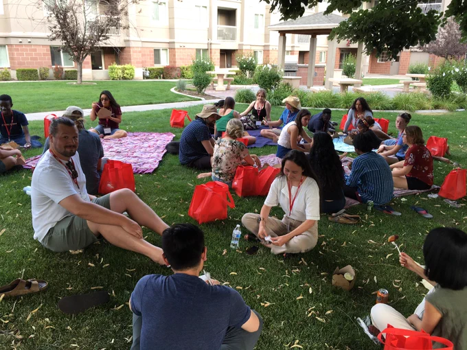 A group of graduate students and instructors sitting on blankets on the grass, having a picnic, talking, and laughing.