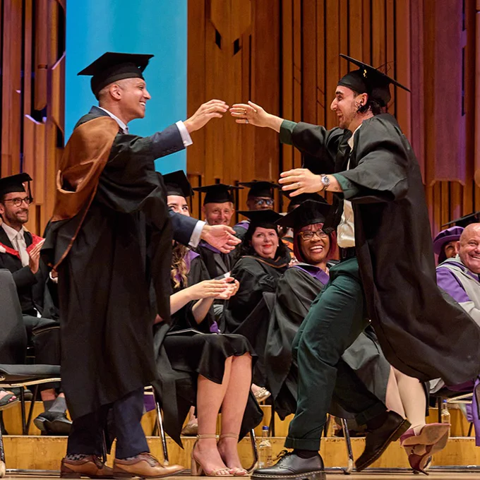 Two graduates joining for a hug on stage