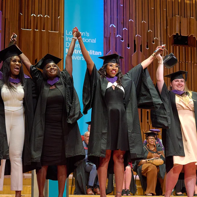 Four graduates holding hands in the air on stage