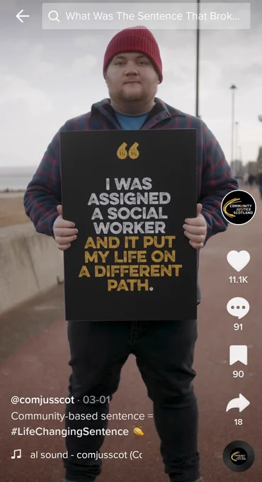 A man on a beach boardwalk holding a sign that says "I was assigned a social worker. And it put my life on a different path."