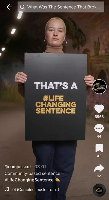 A woman standing in a tunnel holding a sign that reads "That's a #LifeChangingSentence"