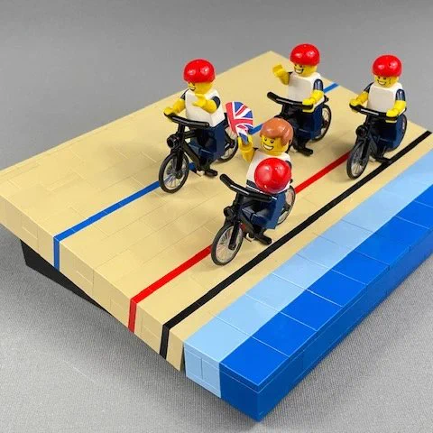 Four lego team GB cyclists on a lego banked cycling track. One cyclist is waving a Union Jack