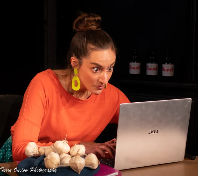 A woman in an orange top looks anxiously at a laptop.