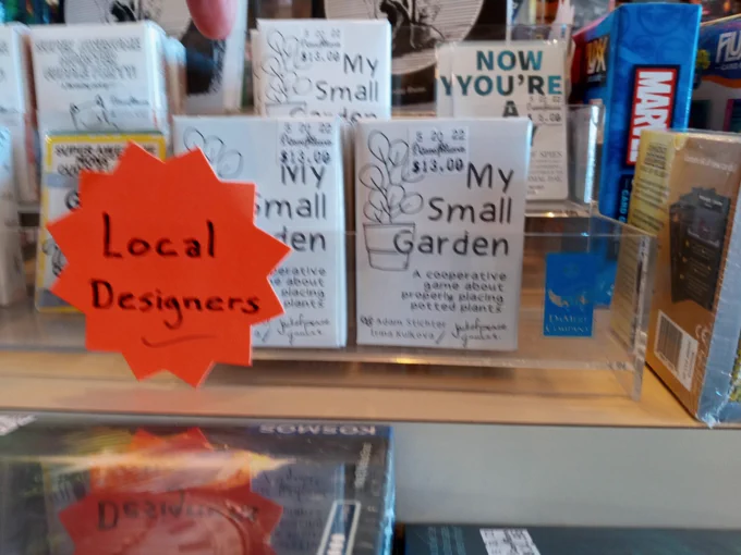 This picture shows a shelf from a board game store. It shows a few small tabletop games including one 
My Small Garden, that is pocket sized. It is designed by Adam Stichter and is featured as one of the games designed by a local designer.