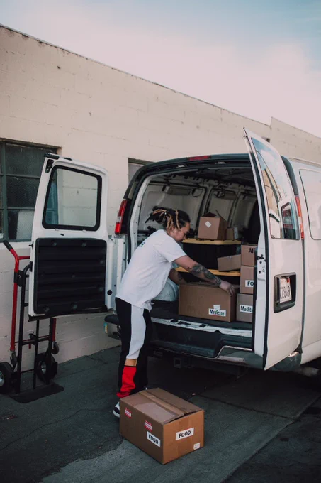 A charity worker loads boxes of food and provisions from the back of a white van