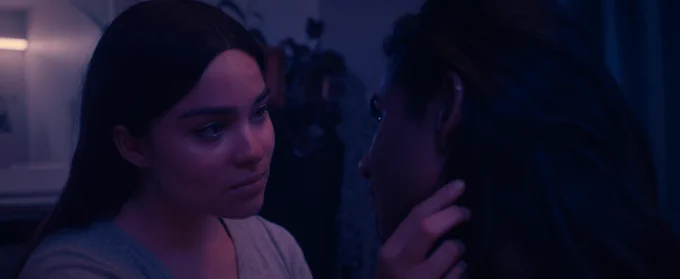 Devery Jacobs holds Priya Guns' face in a dimly lit room in a still from This Place.
