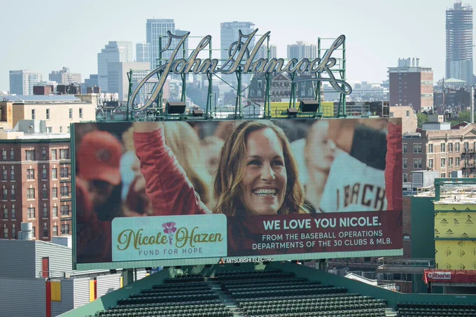 A photo of Nicole Hazen smiling and waving is shown on the Fenway video boards. The video board includes the “Nicole Hazen Fund for Hope” logo and the text “We love you Nicole, from the Baseball Operations Departments of the 30 Clubs & MLB.”