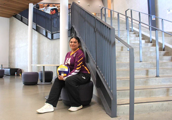 Student seated with volleyball by stairs