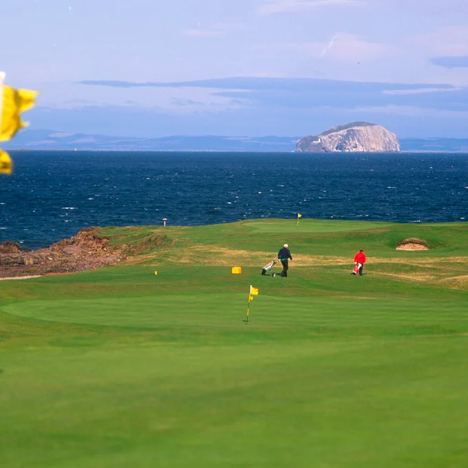 Golfers walk between holes at the winter field golf club with a view to the firth of forth and the bass rock
