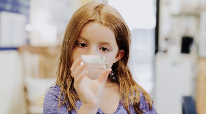 Photograph of young female student with light skin and red hair pondering the volume measurement of a small prism, which she holds in her right hand.