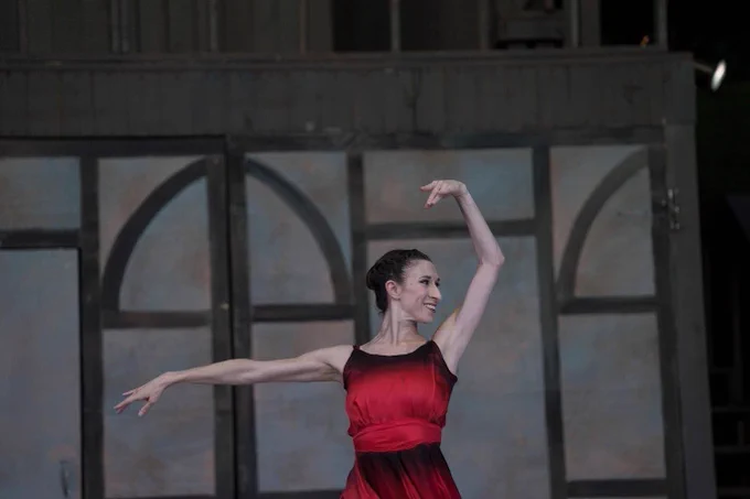 A ballet dancer performs, looks to her left just past her raised arm. She is smiling.