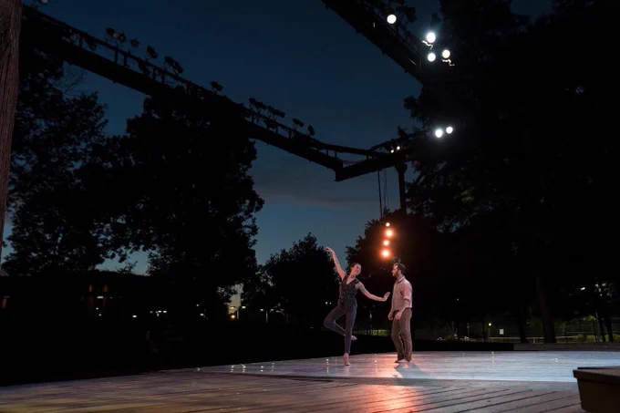 Two dancers perform on an outdoor stage under a night sky.