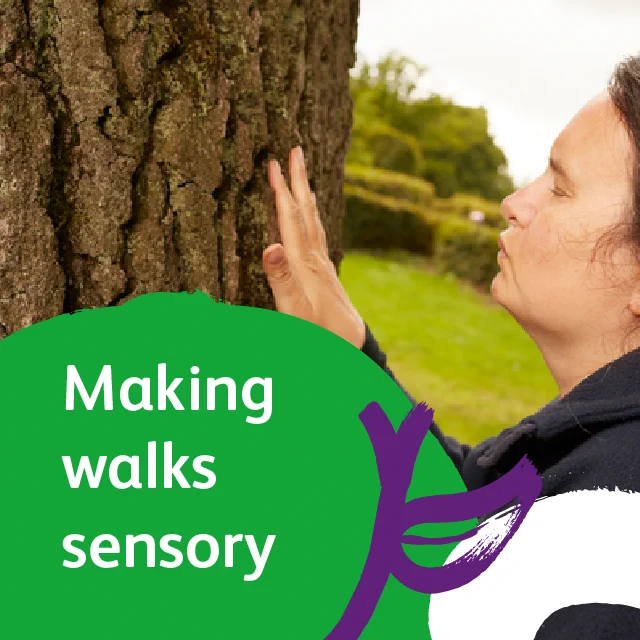 A lady feels the the trunk of a tree during a sensory walk. Her eyes are closed and she has one hand on the tree in a green outdoor space. Over the image is a green circular text box with the words 'making walks sensory' in white text and a purple illustration of a leaf. 