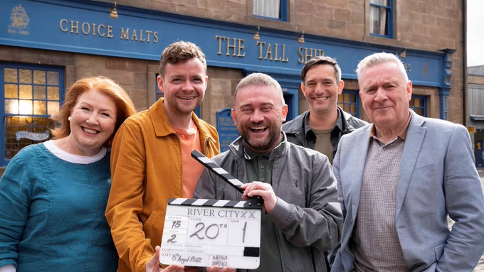 picture shows 5 cast members of River City standing outside the Tall Ship, holding a clapper board that says River City 20th.