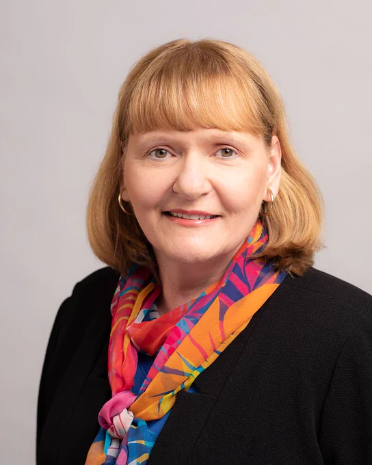 A portrait of Stephanie Urchick smiling and wearing dark top and a colorful scarf.