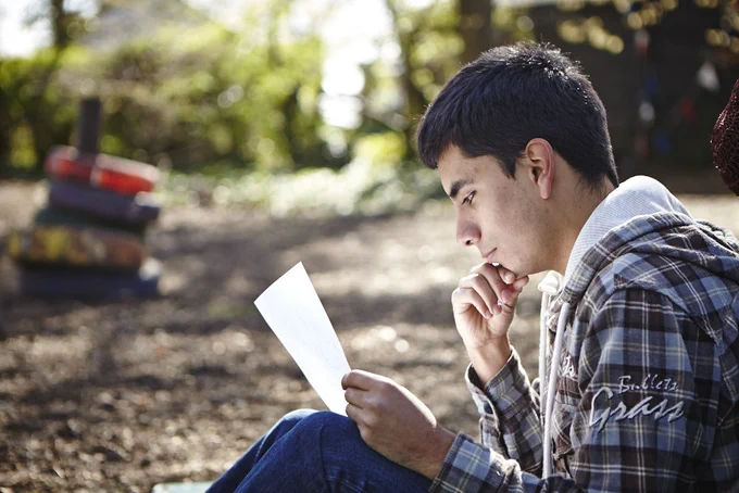 Explorer reading a piece of paper whilst sat outside on the ground