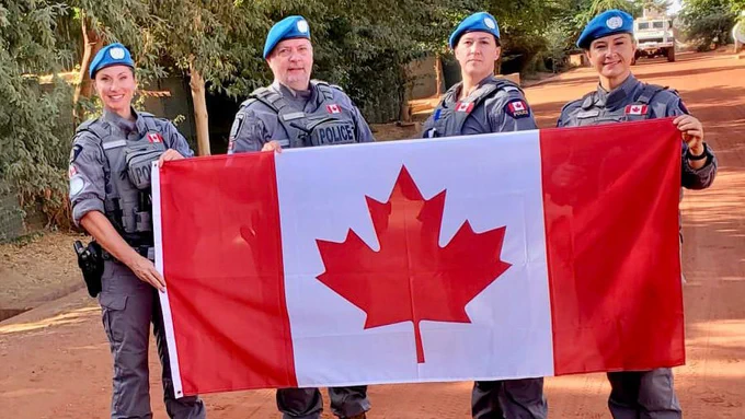 4 Canadian police officers stand together holding a Canadian flag while smiling at the camera outside in Mali.