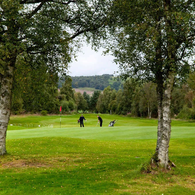 Image shows two golfers, one chipping from off the green, at Alyth Golf Club, Perthshire