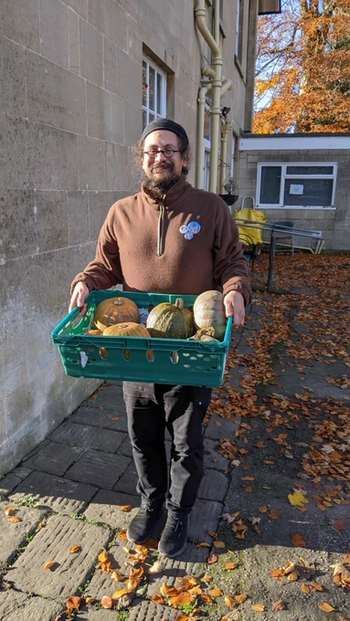 A staff member smiling whilst holding a crate of donated pumpkins and standing outside BEMSCA at Fairfield House in Bath.