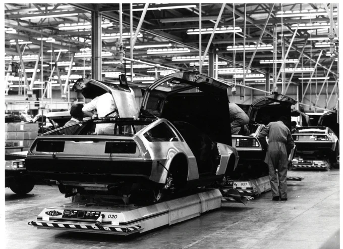 B&W photograph of DeLorean cars being manufactured in a factory.