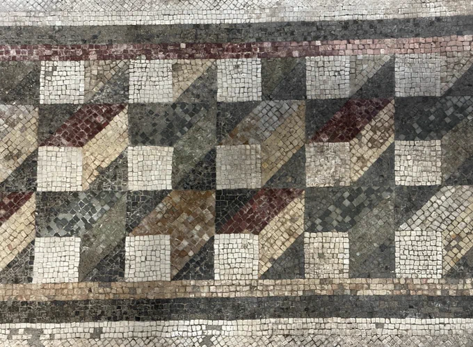 Mosaic seen from above made up of representations of boxes in perspective with alternating red, green, and yellow sided boxes with white ends