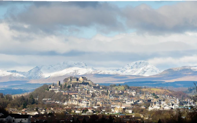 A longview of Stirling town with the Castle at the top. In the background are snow-covered mountains.