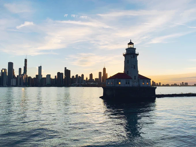 Skyline view of Chicago from the water at sunset, with the Chicago Harbor Lighthouse in the foreground.