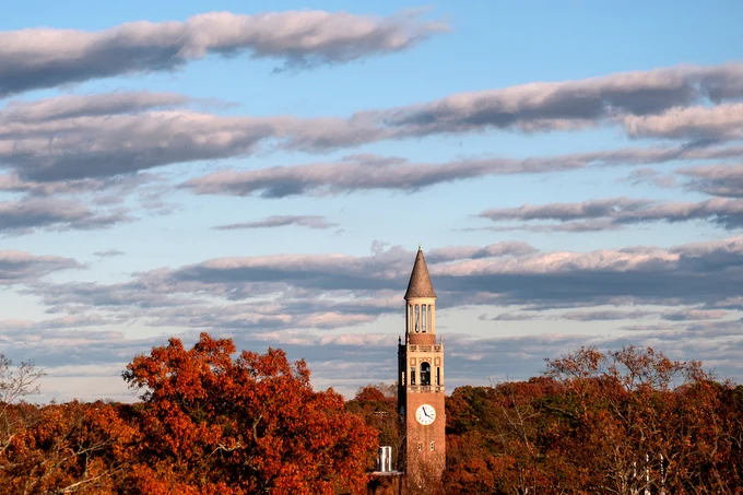 The bell tower under a light blue sky. The surrounding trees are red and orange.