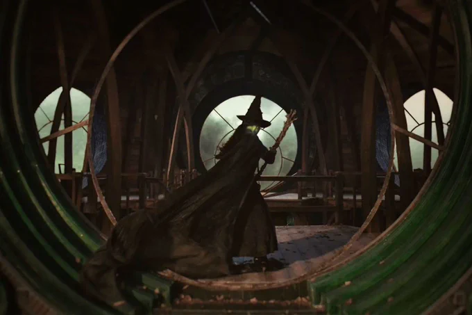 A scene from the film adaptation of Wicked shows Elphaba in a black cape and dress and pointed hat.